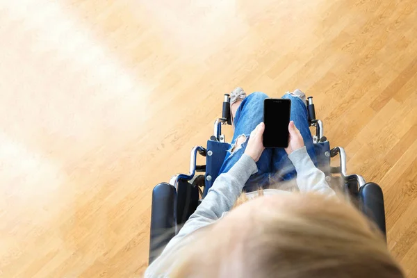Mujer discapacitada en silla de ruedas usando smartphone. Vista superior, maqueta — Foto de Stock