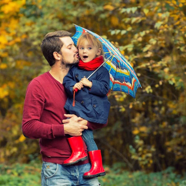 Papá tiene a una hija en las manos en un parque de otoño. Impermeable, goma —  Fotos de Stock