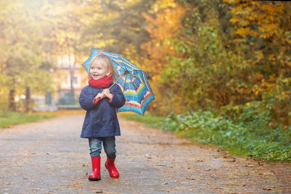 Uma menina pequena vestida com botas de borracha e capas de chuva, segura uma coruja — Fotografia de Stock