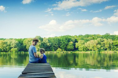 Baba ve dungarees küçük bir kız köprü üzerinde oturuyorlar bir