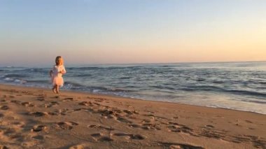 Gün batımında küçük bir kız sahilde koşar..