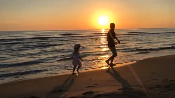Πατέρας και κόρη που τρέχει κατά μήκος της παραλίας στο ηλιοβασίλεμα. — Αρχείο Βίντεο