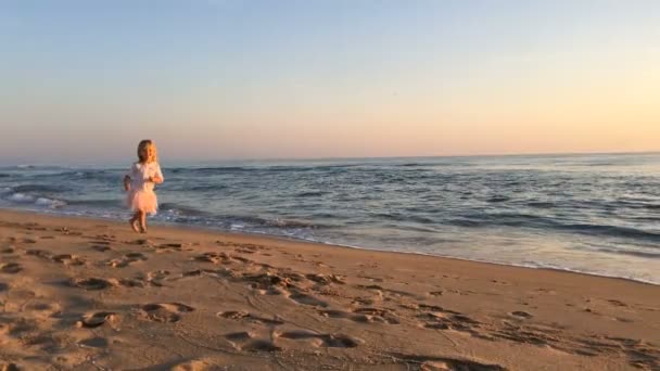 En liten flicka springer längs stranden vid solnedgången. — Stockvideo