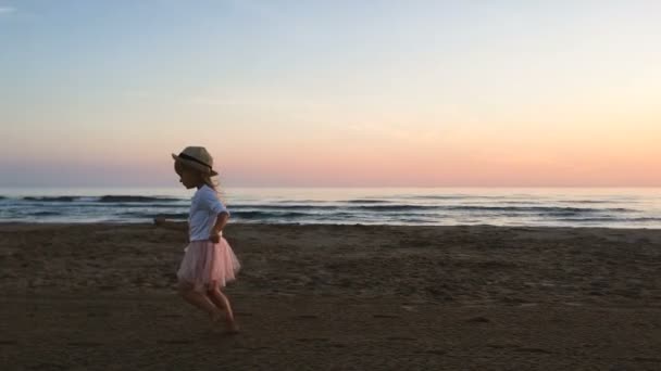 Gün batımında küçük bir kız sahil boyunca koşuyor. Yavaş çekim, siluet video. — Stok video
