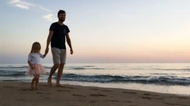 Baba ve kızı gün batımında sahilde koşmak.