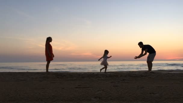 Meisje loopt tussen haar ouders langs het strand bij zonsondergang. — Stockvideo