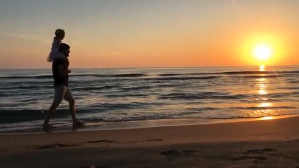 Vater und Tochter laufen bei Sonnenuntergang am Strand entlang. — Stockvideo