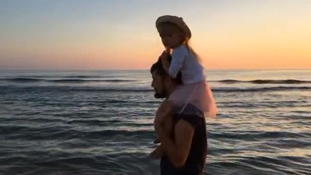 Vader en dochter lopen langs het strand bij zonsondergang. — Stockvideo