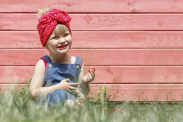 La fille mange des fraises par une journée ensoleillée. elle sourit et a l'air — Photo