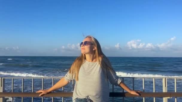 Jovem mulher está olhando para o sol à tarde, fundo ondas do mar . — Vídeo de Stock