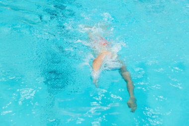 Genç bir çocuk havuza atlıyor..