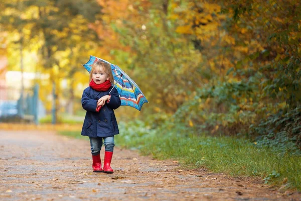 O fetiță îmbrăcată în cizme de cauciuc și haine de ploaie, deține un deget mare — Fotografie, imagine de stoc