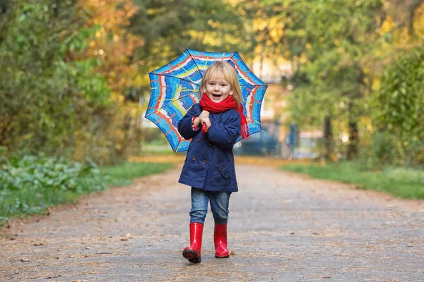 En liten flicka klädd i gummistövlar och regnrockar, håller en tumme — Stockfoto