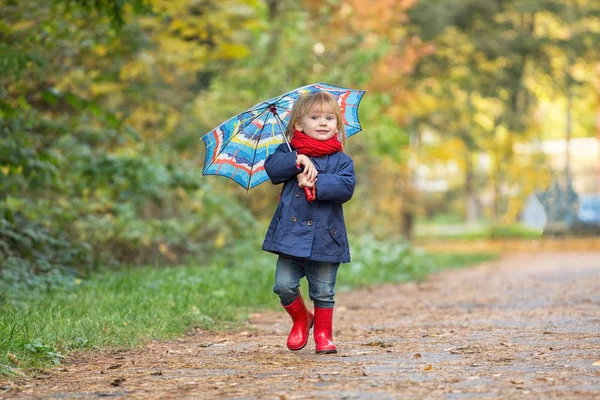 En liten flicka klädd i gummistövlar och regnrockar, håller en tumme — Stockfoto