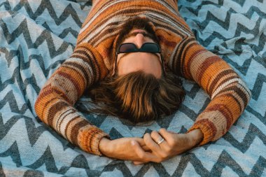 Kazak ve bir battaniye var, açık havada sunrise soğutma güneş gözlüğü uzun saçlı Genç bir yetişkin sakallı adam