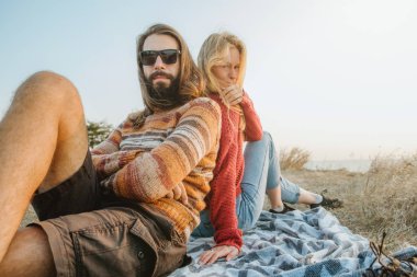 Sarışın kadın ve uzun saçlı esmer adam bir hipster çift soğutma ve battaniye var altın gündoğumu sarılma.