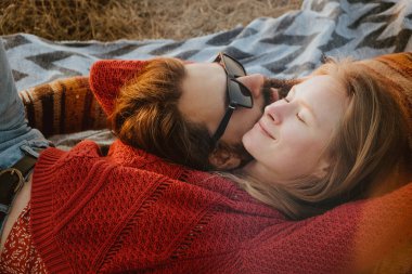 Sarışın bir kadın ve bir battaniye var, açık havada sunrise sarılma ve tüyler ürpertici kazak uzun saçlı esmer adam bir hipster çift.
