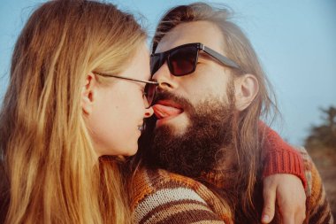 Hipster kaç sarılma ve having fun açık havada gündoğumu içinde güneş gözlüğü içinde gülümseyen. Sakallı adam ve sarışın kadın.