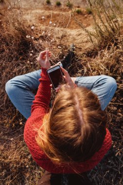 Kayalık bir kıyısında çiçek resimleri alarak bir kırmızı kazaklı genç zencefil kız fotoğrafçı.