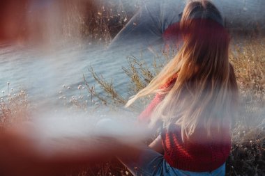 Bir kayalık sahil deniz kenarında bir kırmızı kazaklı sigaranın altın Sunrise bir genç asi gingergirl.