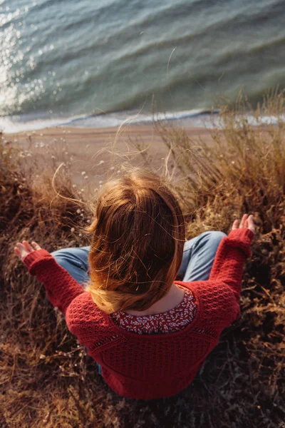 一个年轻的冷静姜女孩在红色毛衣沉思在岩石海岸与尼斯海景 — 图库照片