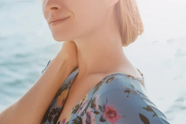 Close-up ortrait of a young beautiful graceful and naturally blond woman in blue dress with sea in background