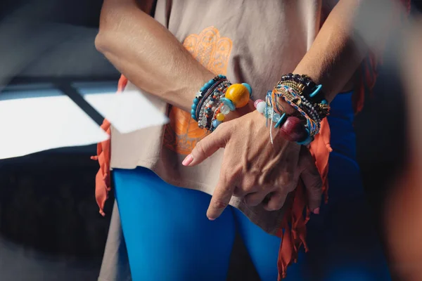 Hands of a mature woman with colorful accessories on wrists and colorful clothes.