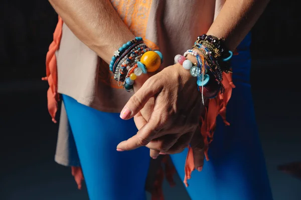 Hands of a mature woman with colorful accessories on wrists and colorful clothes.