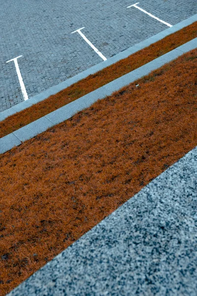Conceprual diagonal shot of grey parking space contrasting with orange burned autumn grass