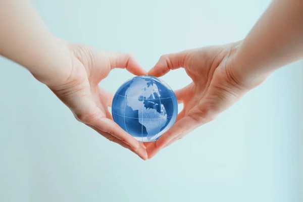 Hands in shape of heart  holding blue glass globe of South and N