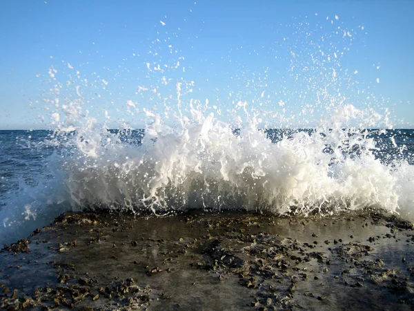 Heldere spatten van de golven van de zee op de oude stenen Pier op een zonnige dag. — Stockfoto