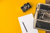 Psací stroj, Vintage Film fotoaparát, list papíru a tužku na žlutém pozadí, pohled shora. Tvůrčí psaní koncept