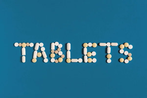 Global Medicine And Health Care Pharmacy Concept. Word Tablets Is Lined With White Pills On A Blue Background, Top View