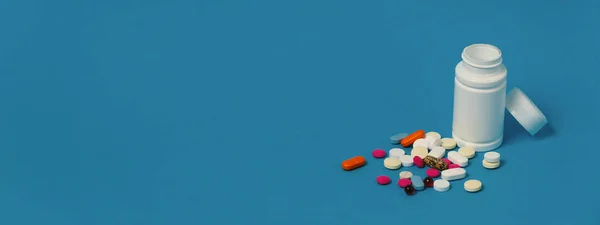 Global Medicine Healthcare Pharmacy Concept. Multicolored Pills And White Bottle On Blue Surface.