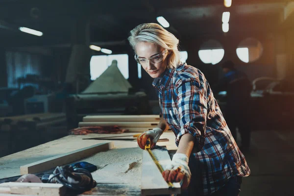 Beautiful woman carpenter designer works with ruler, make notches on the tree in workshop.  Image of modern femininity. Concept of professionally motivated women