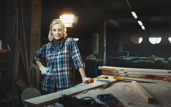 Schöne Arbeiterin mittleren Alters posiert vor dem Hintergrund einer Holzwerkstatt. Konzept motivierter Frauen, Gleichberechtigung der Geschlechter, Bild von Weiblichkeit in der modernen Welt — Stockfoto