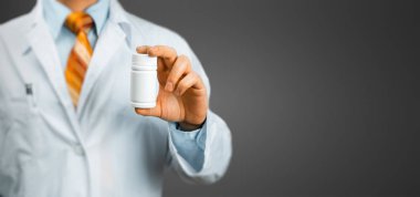 Bir kutu hap gri arka plan üzerinde parmaklarını arasında tutan doktor. Sağlık, tıp, sigorta kavramı