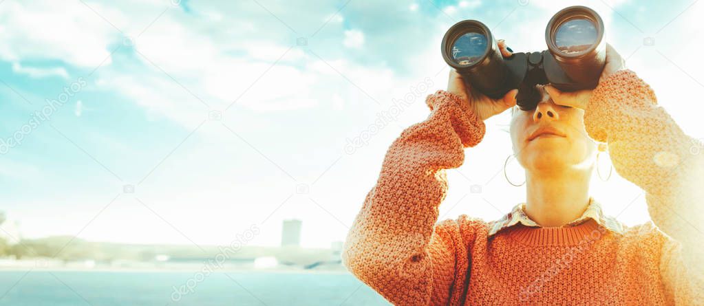 Young girl looks through binoculars at the sea on a bright sunny day. Travel Concept