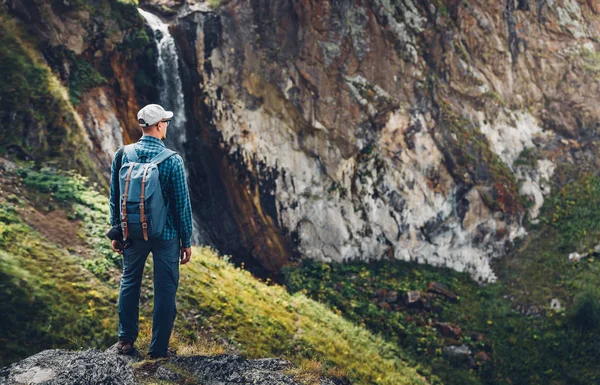 Homem jovem viajante em pé no topo do penhasco em montanhas e apreciando vista da natureza, vista traseira com espaço de cópia — Fotografia de Stock