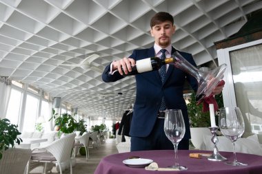 Genç erkek sommelier kırmızı şarap tadımı sırasında bir sürahi dökme