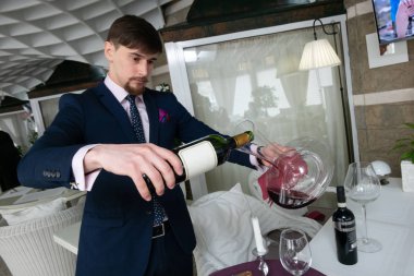 Genç erkek sommelier kırmızı şarap tadımı sırasında bir sürahi dökme