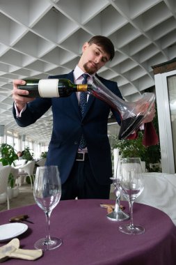 Genç erkek sommelier kırmızı şarap tadımı sırasında bir sürahi dökme