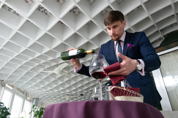the young male sommelier pouring red wine into a decanter while tasting