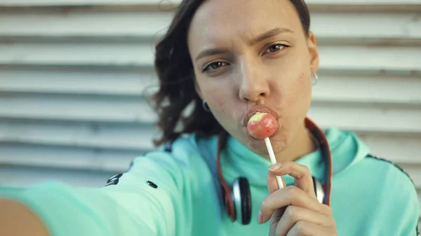 Girl licking lollipop and making selfie using smartfone — Stock Photo, Image