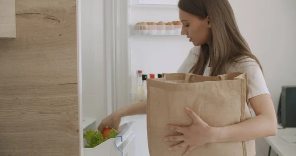 Mladá žena vybaluje potravinový sáček do ledničky — Stock fotografie