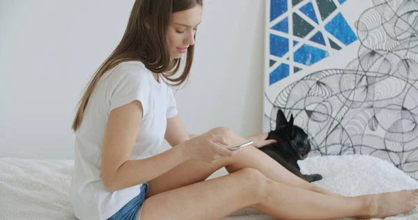 Chica acostada en la cama en casa y mensajes de texto en su teléfono — Foto de Stock