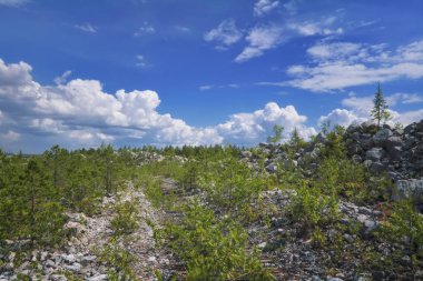 Beyaz kümülüs bulutları ile mavi bir yaz gökyüzüne karşı büyük taşlar ile dağ yamacı.