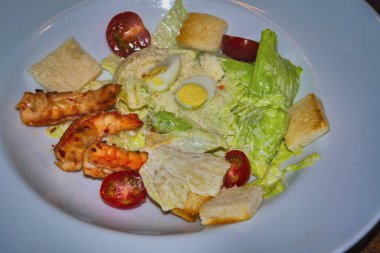 Sezar salatası ve karidesler beyaz bir tabakta. Üstte görüntü.