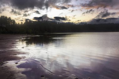 Berrak şeffaf mavi su ile bir orman gölü kıyısında Yaz manzara. Günbatımı.