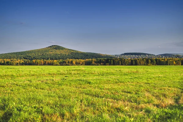 Landsbygdslandskap nyklippt äng mot bakgrund av skogen och bergen vid horisonten. Tidig höst. — Stockfoto